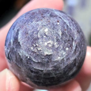 May include: A smooth, round, purple and grey gemstone with a swirling pattern.
