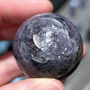 May include: A dark purple and silver sphere with a textured surface. The sphere is made of natural stone and has a unique, swirling pattern.