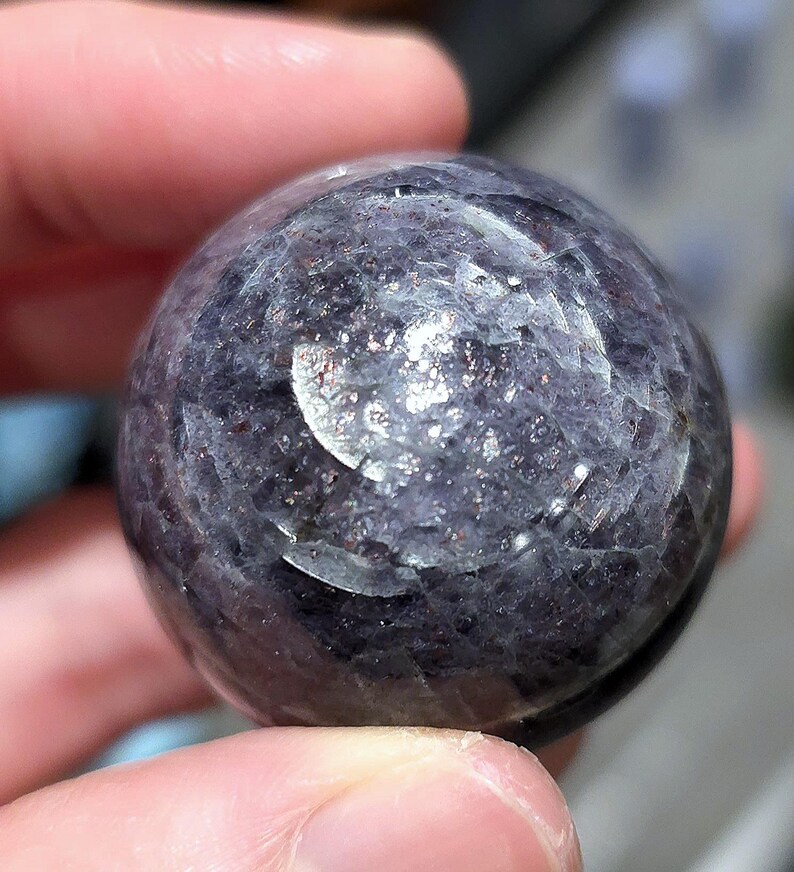 May include: A dark purple and silver sphere with a textured surface. The sphere is made of natural stone and has a unique, swirling pattern.