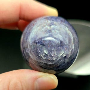 Puede incluir: Una esfera de piedra preciosa redonda, lisa, de color p&uacute;rpura y azul con un patr&oacute;n de remolino.