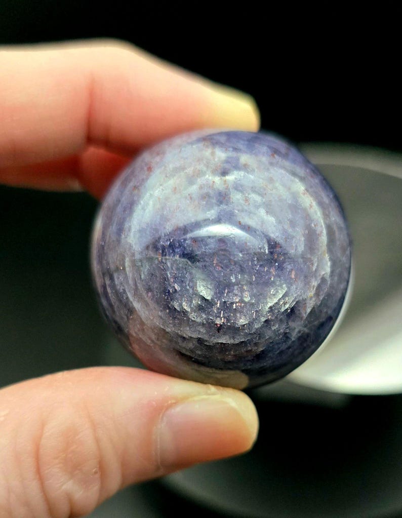 Puede incluir: Una esfera de piedra preciosa redonda, lisa, de color p&uacute;rpura y azul con un patr&oacute;n de remolino.