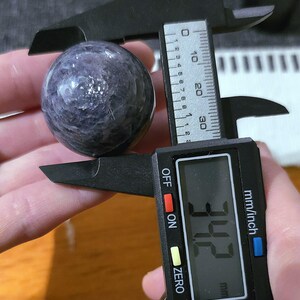 May include: A purple and white sphere with a diameter of 3.42 inches, measured with a digital caliper.