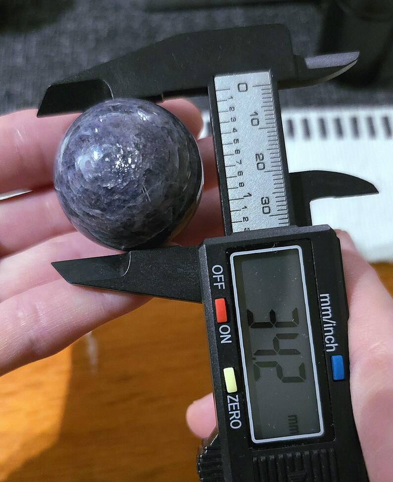 May include: A purple and white sphere with a diameter of 3.42 inches, measured with a digital caliper.