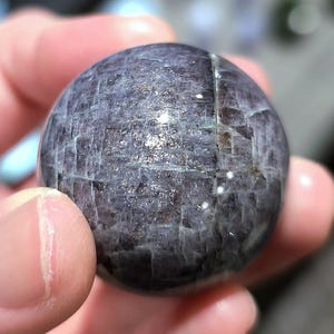 May include: A smooth, round, dark gray and silver sphere with a textured surface. The sphere is made of a natural material, possibly a crystal or gemstone.