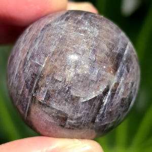 Puede incluir: Una esfera de piedra preciosa redonda, lisa, de color p&uacute;rpura y gris con un patr&oacute;n estriado.