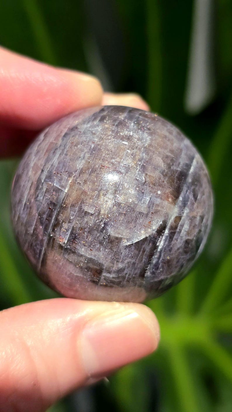 Puede incluir: Una esfera de piedra preciosa redonda, lisa, de color p&uacute;rpura y gris con un patr&oacute;n estriado.