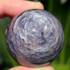 Puede incluir: Una esfera de piedra preciosa redonda, lisa, de color p&uacute;rpura y gris con un patr&oacute;n de remolino.