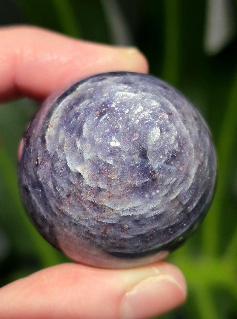 Puede incluir: Una esfera de piedra preciosa redonda, lisa, de color p&uacute;rpura y gris con un patr&oacute;n de remolino.