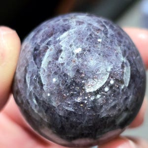 May include: A smooth, round, purple and silver gemstone sphere. The sphere has a swirling pattern of silver and purple.
