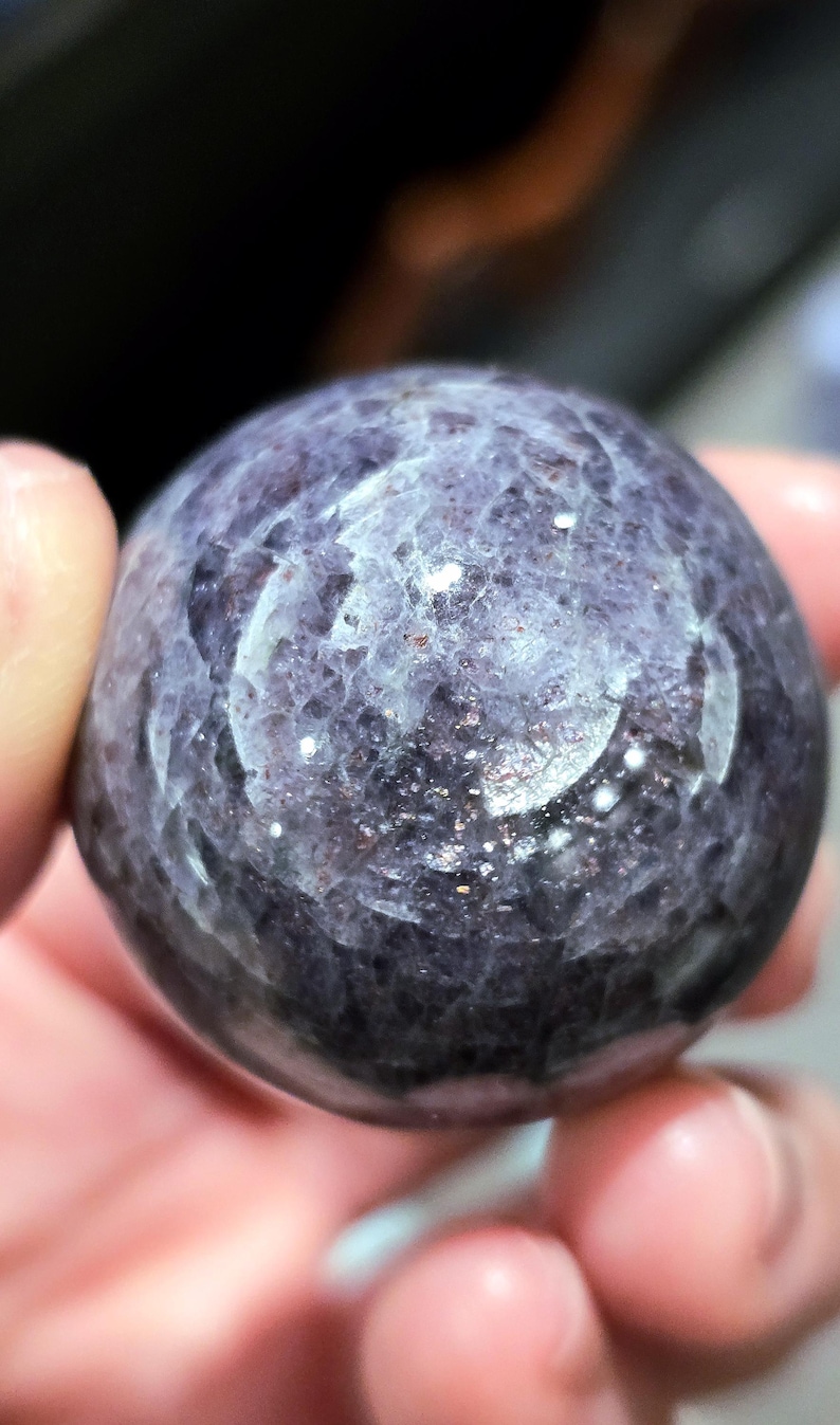 May include: A smooth, round, purple and silver gemstone sphere. The sphere has a swirling pattern of silver and purple.