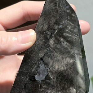 May include: A dark, triangular crystal with a polished surface. The crystal is primarily black with subtle grey and white veining, and a small, irregular cavity. The shape is reminiscent of a pyramid, suitable for display or collection.