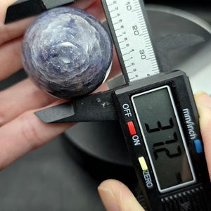 Puede incluir: Primer plano de una esfera de piedra preciosa azul y morada que se mide con un calibre digital. El calibre indica 37,2 mm.