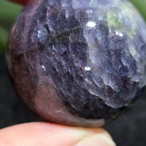 K&ouml;nnte beinhalten: Eine glatte, runde, violette und graue Edelsteinkugel. Die Kugel hat ein gestreiftes Muster und einen leichten Glanz.