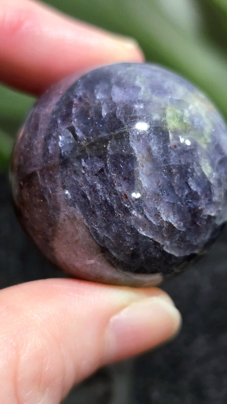 K&ouml;nnte beinhalten: Eine glatte, runde, violette und graue Edelsteinkugel. Die Kugel hat ein gestreiftes Muster und einen leichten Glanz.