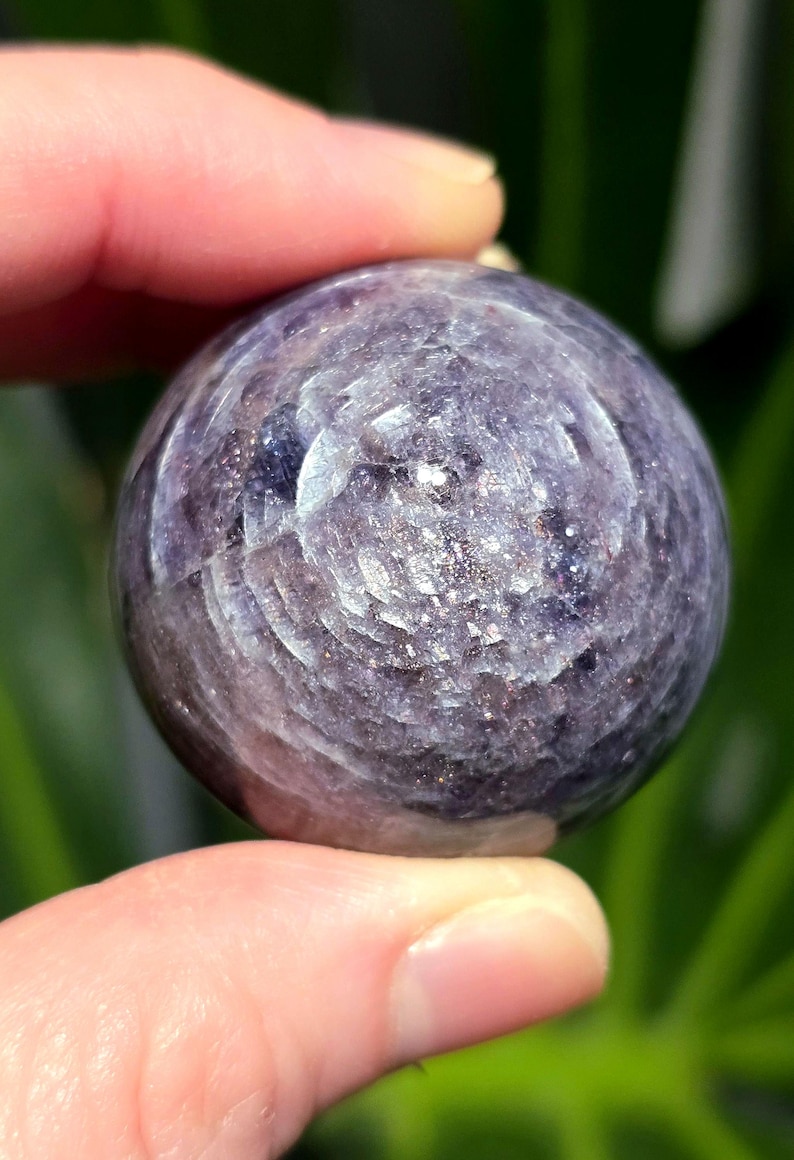 Puede incluir: Una esfera de color p&uacute;rpura y plateado con un patr&oacute;n de remolino. La esfera est&aacute; hecha de piedra natural y es lisa al tacto.