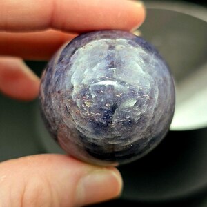 Puede incluir: Una esfera de piedra preciosa redonda, lisa, p&uacute;rpura y gris. La esfera tiene un patr&oacute;n de remolino y un acabado pulido brillante.