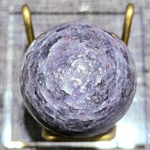 May include: A purple and white gemstone sphere with a swirling pattern, displayed on a gold stand.