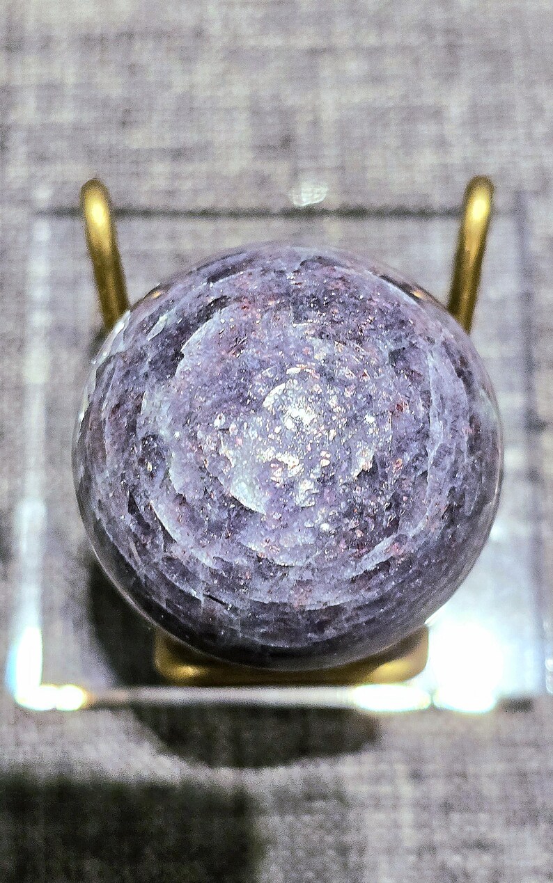 May include: A purple and white gemstone sphere with a swirling pattern, displayed on a gold stand.