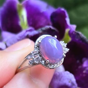 Puede incluir: Un anillo de plata con una gran piedra preciosa ovalada de color púrpura rodeada de pequeñas piedras preciosas transparentes.