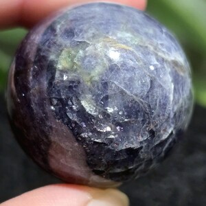 K&ouml;nnte beinhalten: Eine violette und graue Edelsteinkugel mit einer glatten, polierten Oberfl&auml;che. Die Kugel hat ein einzigartiges, wirbelndes Muster aus hellen und dunklen Farbt&ouml;nen.