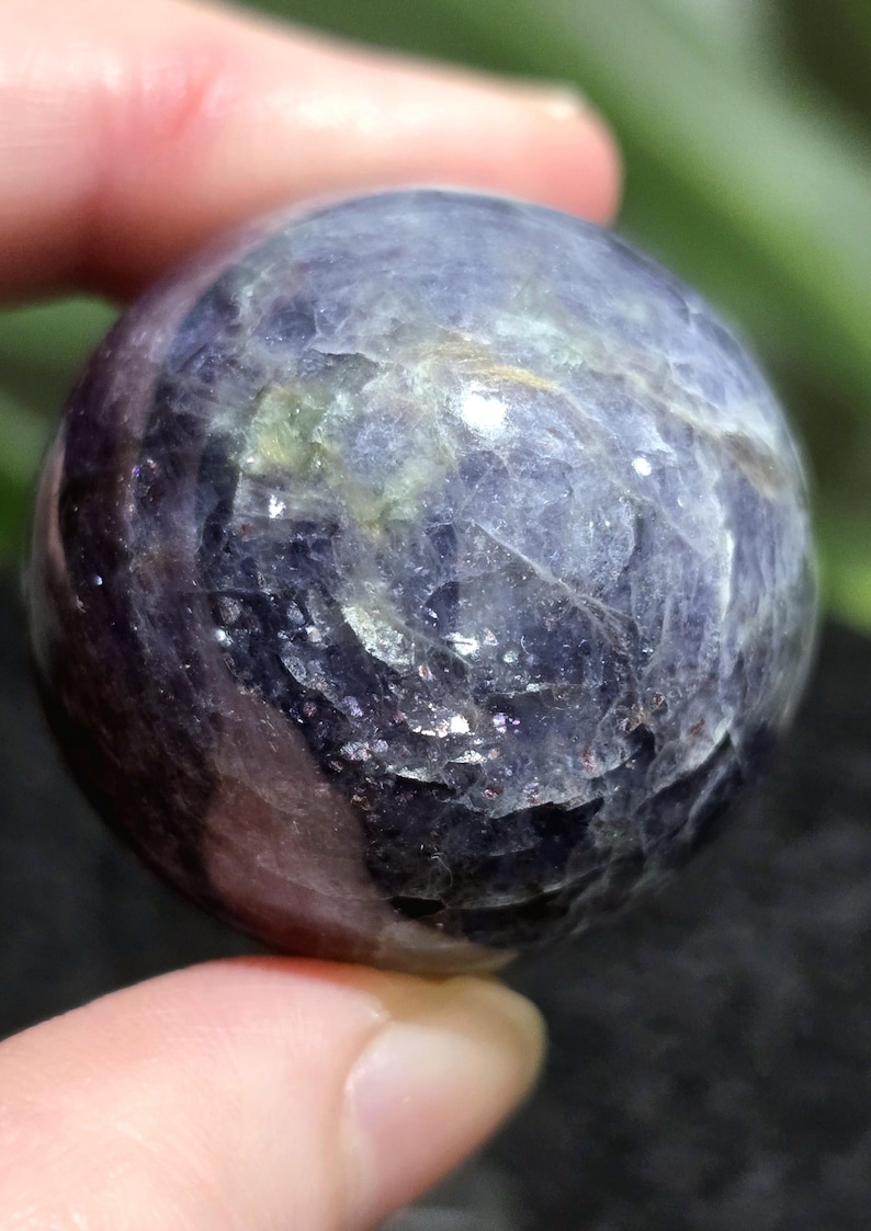 K&ouml;nnte beinhalten: Eine violette und graue Edelsteinkugel mit einer glatten, polierten Oberfl&auml;che. Die Kugel hat ein einzigartiges, wirbelndes Muster aus hellen und dunklen Farbt&ouml;nen.