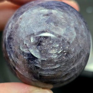 Puede incluir: Una esfera de piedra preciosa redonda y lisa, de color p&uacute;rpura y gris. La esfera tiene un patr&oacute;n de remolino de tonos claros y oscuros.