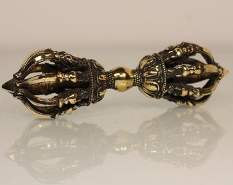 May include: A gold and black metal vajra, a ritual object used in Buddhism and Hinduism. The vajra is a double-headed thunderbolt, symbolizing strength and power.