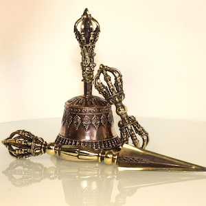May include: A bronze bell with detailed patterns and a decorative handle, alongside two ornate, gold-toned ritual objects. The bell and objects are likely used for spiritual or ceremonial purposes.