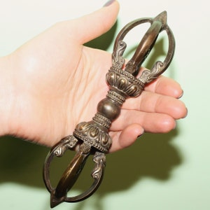 May include: A bronze Tibetan ritual vajra, also known as a dorje, with intricate details and a pointed tip. The vajra is a symbol of strength, power, and enlightenment in Buddhism.
