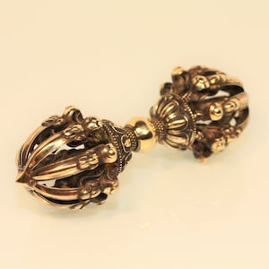 Peut inclure: Un vajra en métal doré, une arme rituelle du bouddhisme, avec des détails complexes et une pointe pointue. Le vajra est un symbole de force, de pouvoir et d'illumination.