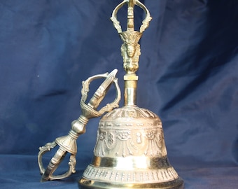 May include: A gold-colored Tibetan bell and a matching hand-held vajra, a ritual implement used in Buddhism. The bell is decorated with intricate designs and the vajra has a face on the top.