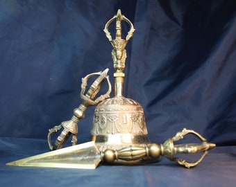 May include: A set of three golden Tibetan ritual objects: a bell, a dorje, and a vajra. The bell is decorated with intricate carvings and the dorje and vajra have ornate handles.