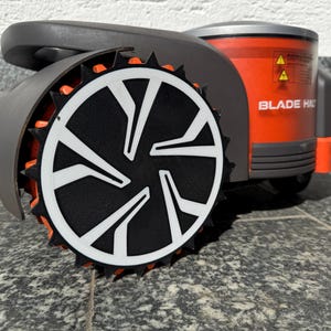 Könnte beinhalten: Ein Mähroboter mit einem dunkelgrauen und orangefarbenen Gehäuse und einem markanten schwarz-weißen Zahnrad. Die Seite des Geräts zeigt orangefarbene Paneele und ein Warnschild mit dem in weißen Großbuchstaben gedruckten Text BLADE HAZARD.
