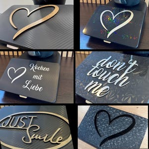 May include: A collection of decorative black square plates with various designs. One features a wooden heart, another a holographic heart, and others have text like "Don't Touch Me" and "Just Smile".