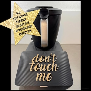 以下が含まれることがあります： シルバーのハンドルが付いた黒いキッチン家電と、木製の文字で「don't touch me」という言葉。ドイツ語のテキストが入った金の星が左側にあります。