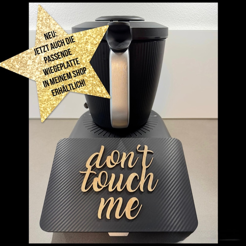 以下が含まれることがあります： シルバーのハンドルが付いた黒いキッチン家電と、木製の文字で「don't touch me」という言葉。ドイツ語のテキストが入った金の星が左側にあります。
