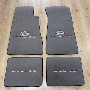 Könnte beinhalten: Ein Set aus vier dunkelgrauen Automatten mit schwarzer Umrandung. Die beiden vorderen Matten zeigen ein gesticktes Impala SS-Logo mit einem silbernen springenden Hirsch-Emblem. Die beiden hinteren Matten tragen den gestickten Impala SS-Schriftzug.