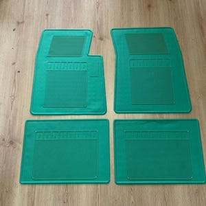 May include: A set of four bright green rubber car floor mats. The two front mats feature a distinct notched corner and a rectangular textured grip area, while the two rear mats are rectangular. All mats have vertical ribbed patterns for traction.