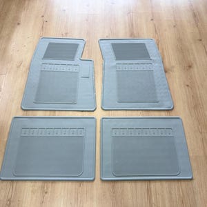 Könnte beinhalten: Ein Set aus vier hellgrauen Automatten. Die beiden vorderen Matten haben eine konturierte Form mit einem rechteckigen, texturierten Griffbereich, während die beiden hinteren Matten rechteckig sind und einen horizontal gerippten Bereich aufweisen.