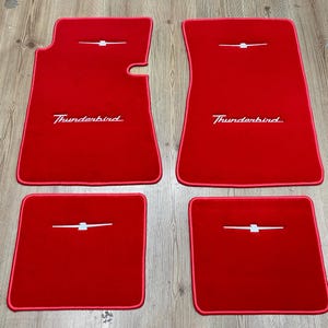 Puede incluir: Un juego de cuatro alfombrillas de coche de color rojo brillante con ribete rojo a juego. Las dos alfombrillas delanteras más grandes presentan el texto Thunderbird bordado en blanco y un emblema de ave blanco, mientras que las dos traseras llevan el emblema.