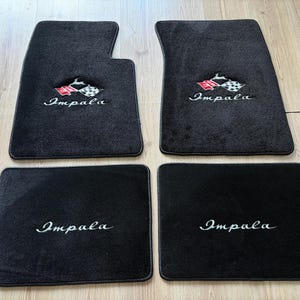 Könnte beinhalten: Ein Set aus vier schwarzen Automatten. Die beiden vorderen Matten zeigen ein gesticktes Impala-Logo mit einem rot-weißen Zielflaggen-Emblem. Die beiden hinteren Matten tragen den weißen, gestickten Schriftzug Impala mittig auf der Oberfläche.