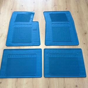 May include: A set of four bright blue car floor mats. The two front mats feature a distinct notched shape at the top, while the two rear mats are rectangular. Each mat includes a textured, ribbed central panel and a smooth border design.