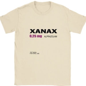 May include: A beige t-shirt with black text that reads "XANAX 0.25 mg ALPRAZOLAM" and "100 Tablets FOR ORAL USE".