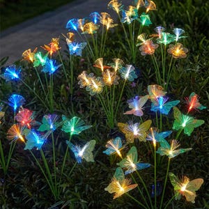 May include: A collection of solar-powered garden lights featuring colorful, illuminated butterflies and flower designs. The lights emit a vibrant glow in shades of blue, green, yellow, orange, and red, creating a decorative outdoor display.