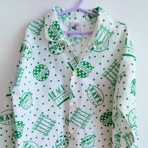 Può includere: Camicia bianca con bottoni, con un motivo a pois verdi e testo verde che dice "Beach Summer", "Navy Team", "Beach" e "Marin".