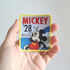 May include: Yellow and red embroidered patch with Mickey Mouse, the text "Mickey '28" and the copyright symbol and the word "Disney".