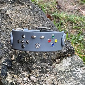 May include: A gray leather dog collar with a gamepad design. The collar is decorated with silver studs and colorful rhinestones.