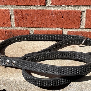 May include: A black rubber dog leash with a silver clip and a textured surface. The leash is coiled on a concrete surface.