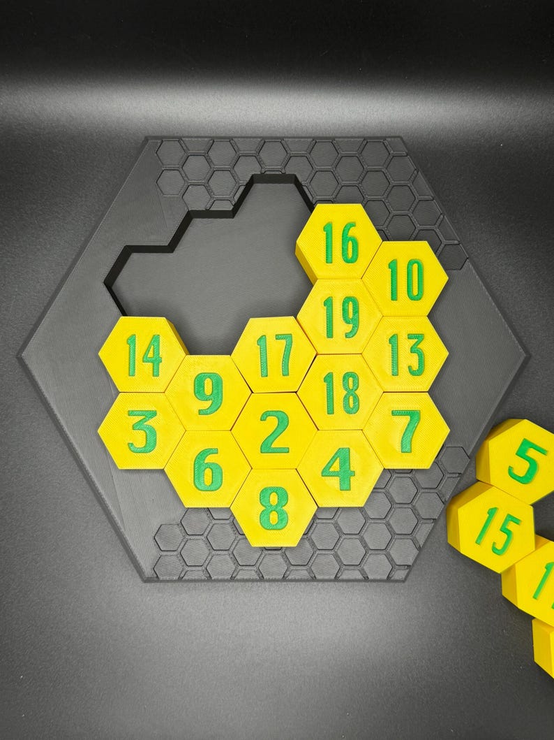 Puede incluir: Un rompecabezas hexagonal amarillo con n&uacute;meros verdes del 1 al 19. Al rompecabezas le falta una pieza. La pieza que falta se muestra a la derecha del rompecabezas.