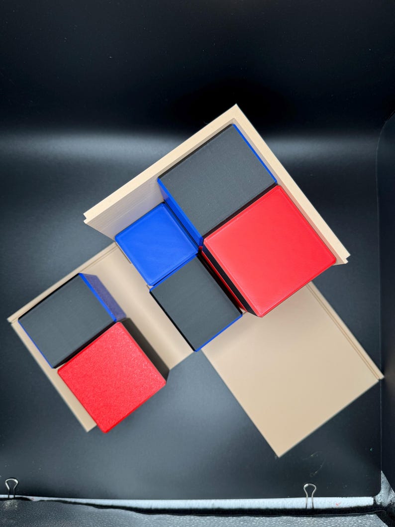 May include: A set of five wooden blocks in various colors, including black, red, and blue. The blocks are arranged in a geometric pattern on a beige surface.